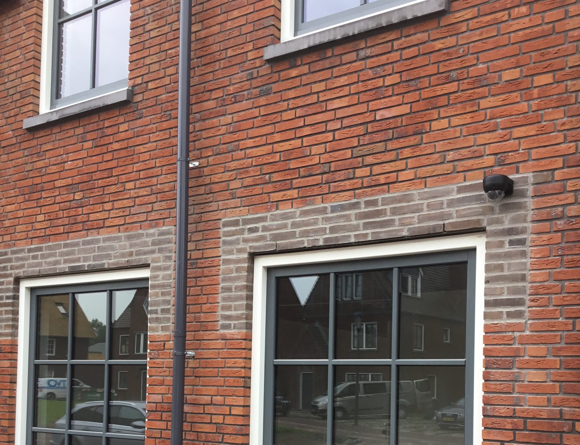 Zwarte domecamera hoog op de bakstenen gevel van een woonhuis boven een raam