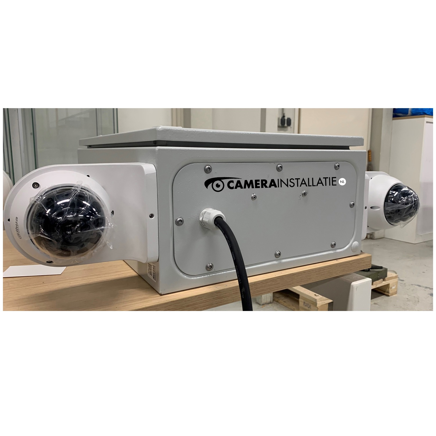 Door CameraInstallatie zelf gebouwde grijze systeemkast met het eigen logo en twee bestuurbare koepelcamera&rsquo;s op armen, klaar op een pallet in het magazijn