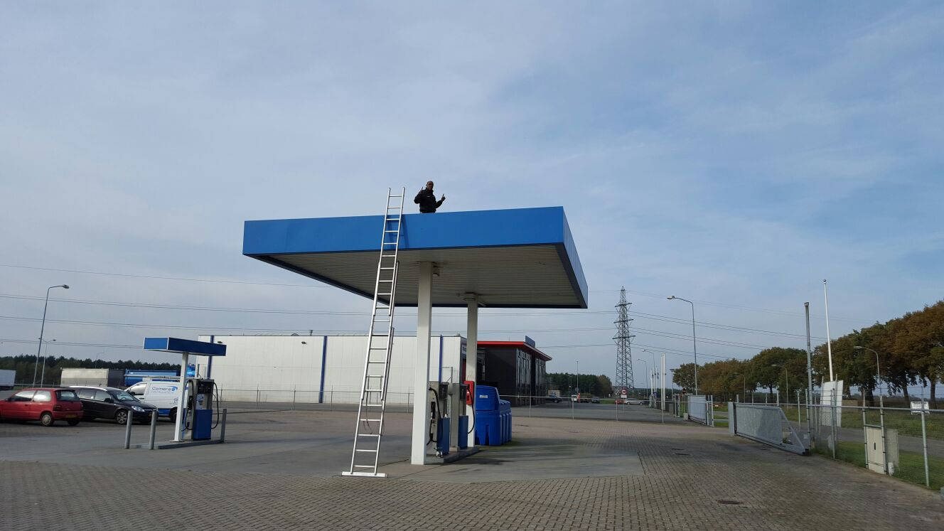 Monteur op het dak van de luifel van een onbemand tankstation, met een ladder tegen de luifel