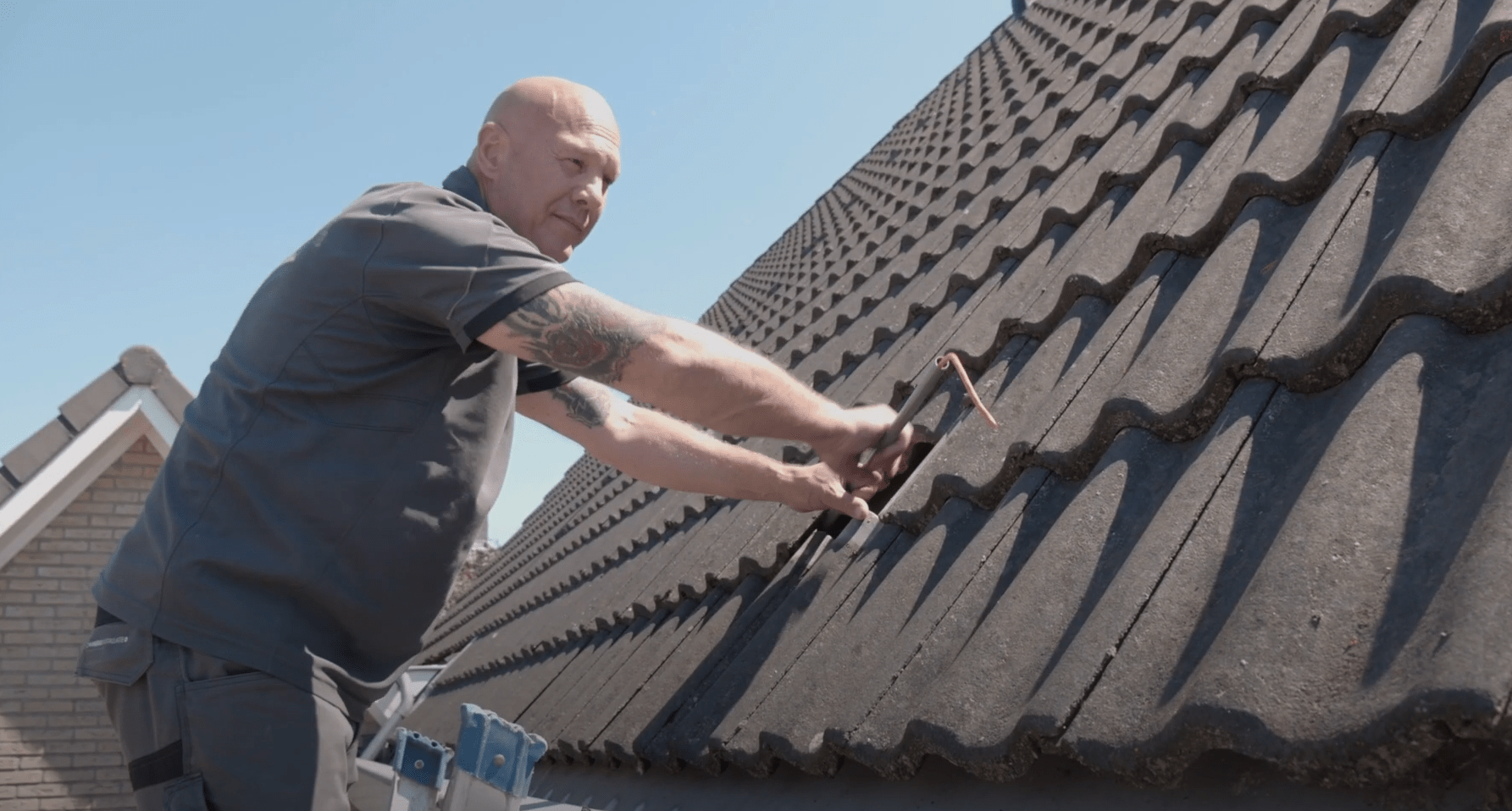 Monteur van CameraInstallatie tilt op een ladder de dakpannen op om een kabel eronder weg te werken