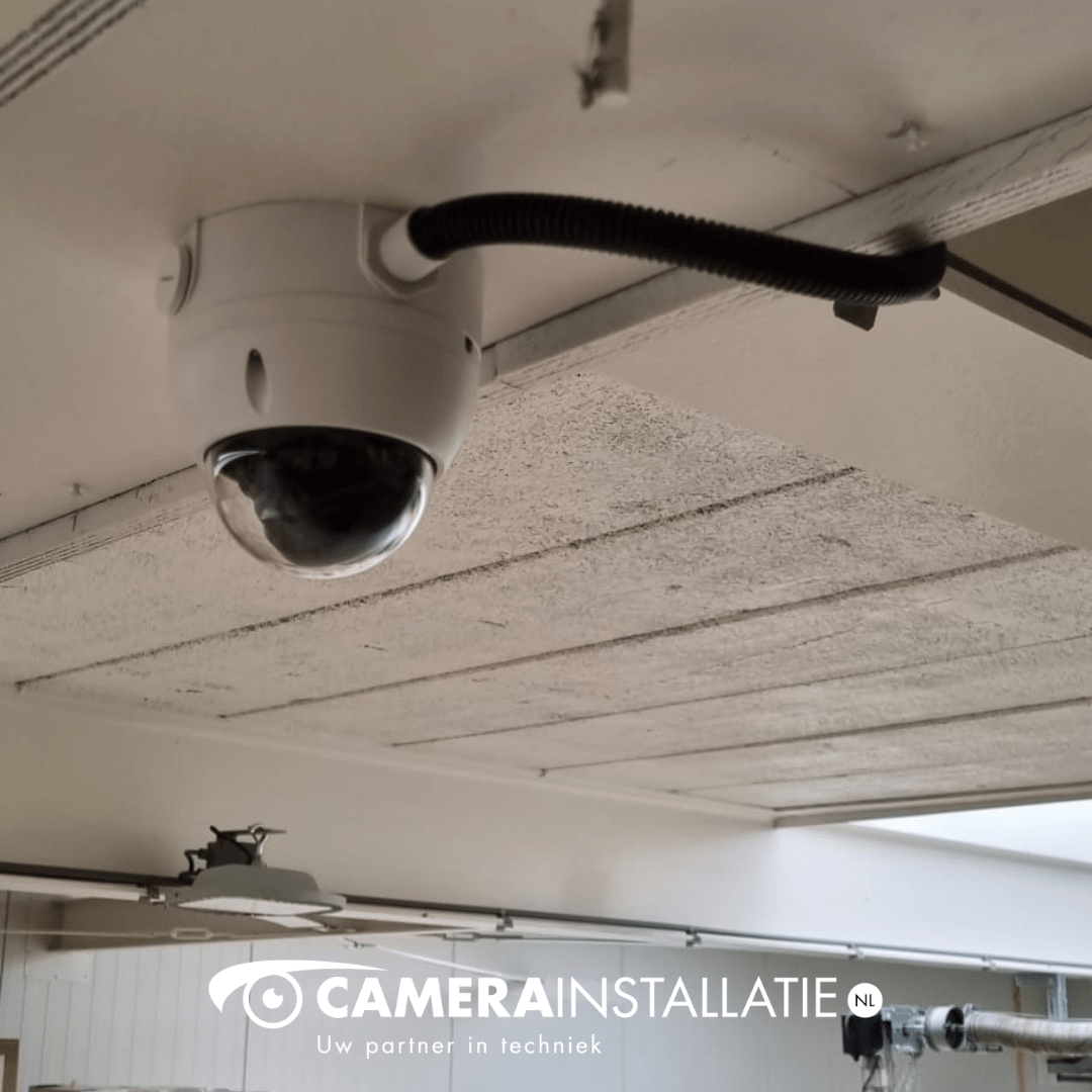 Witte domecamera aan het plafond van een bedrijfsloods, met kabelbuis