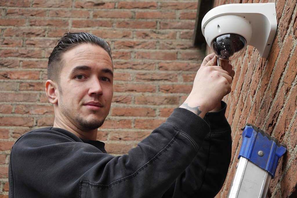 Monteur van CameraInstallatie.nl monteert een witte dome-beveiligingscamera aan een bakstenen buitenmuur
