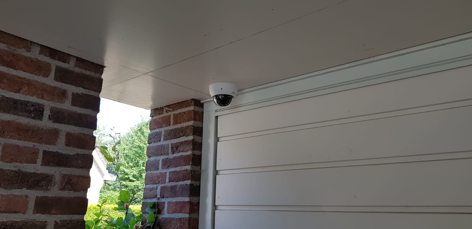 Witte dome-camera onder de overkapping bij een garagedeur van een woning