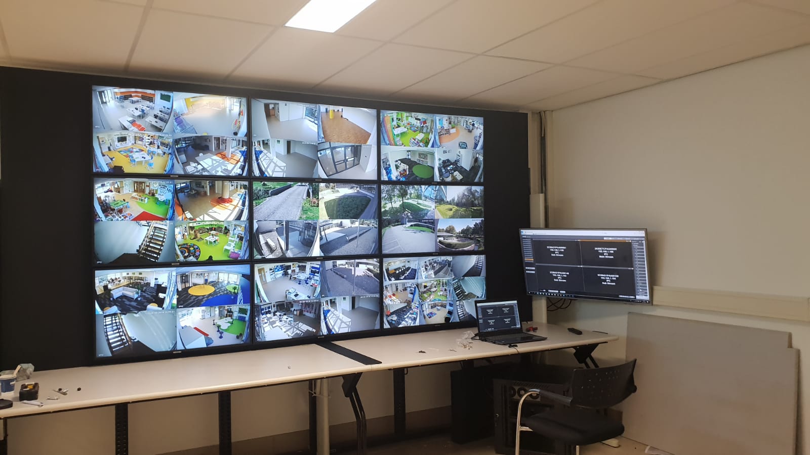 Beeldwand met camerabeelden in een meldkamer, met rechts een losse beheermonitor boven een werktafel