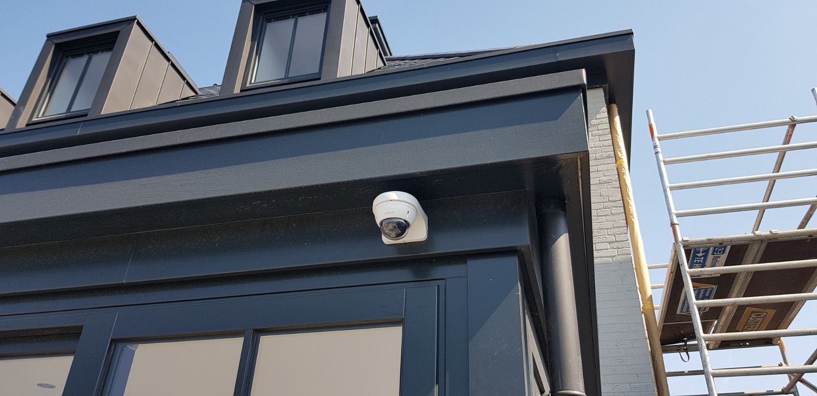 Witte domecamera onder de dakrand van een donkere woning