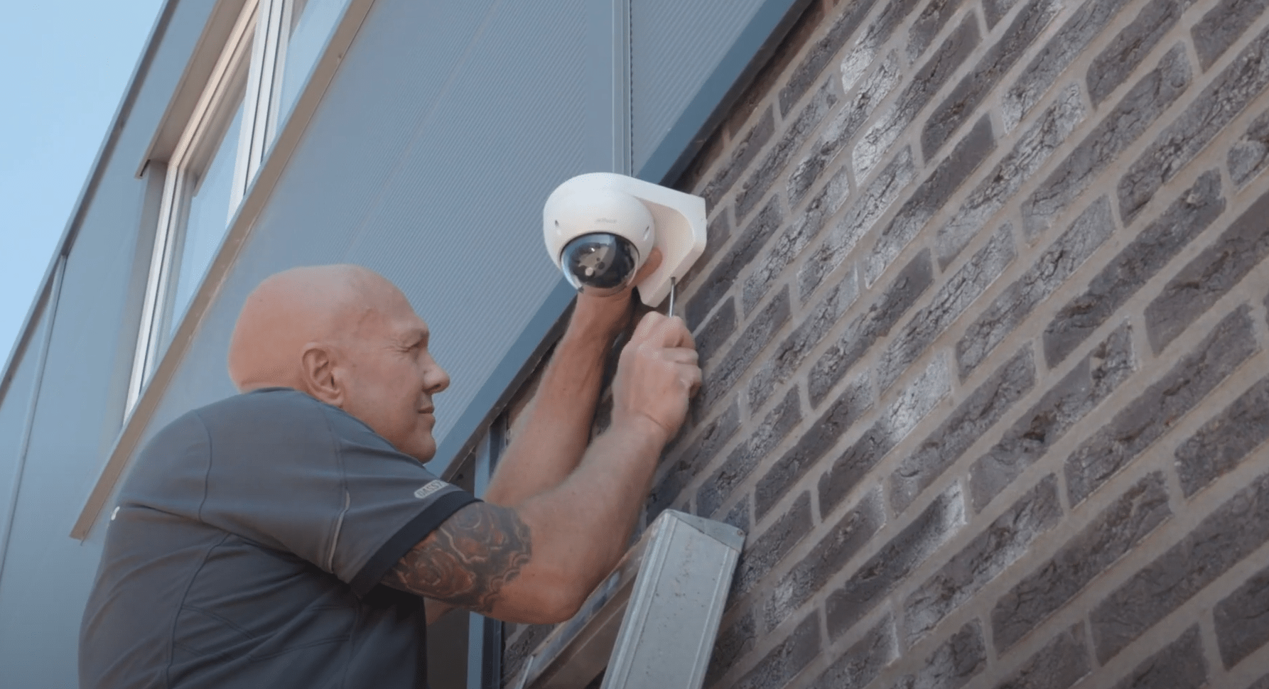 Monteur van CameraInstallatie monteert een witte dome-buitencamera aan de gevel van een pand