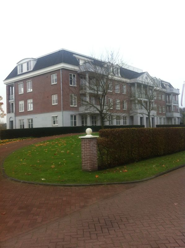 Appartementengebouw van drie lagen met een oprit, haag en gazon ervoor
