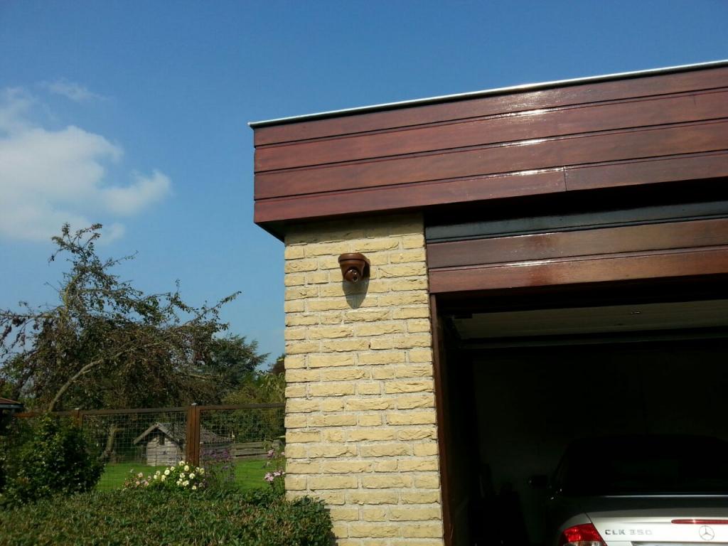 Bruin gespoten dome-camera op de hoek van de garage, onder een donkere houten boeiboord