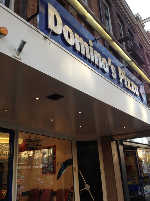 Domecamera boven de entree van de Domino's Pizza-vestiging in Amsterdam, gemonteerd onder de luifel bij de ingang