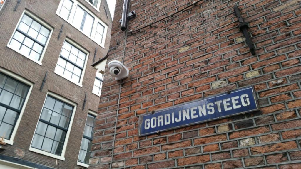 Discrete bewakingscamera aan een monumentale bakstenen gevel in een smalle steeg in het oude centrum van Amsterdam