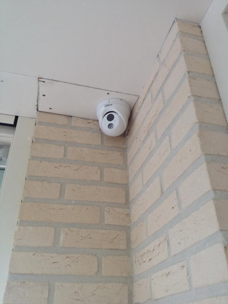 Witte gesloten beveiligingscamera in de hoek onder een overstek bij een woning met lichte baksteen