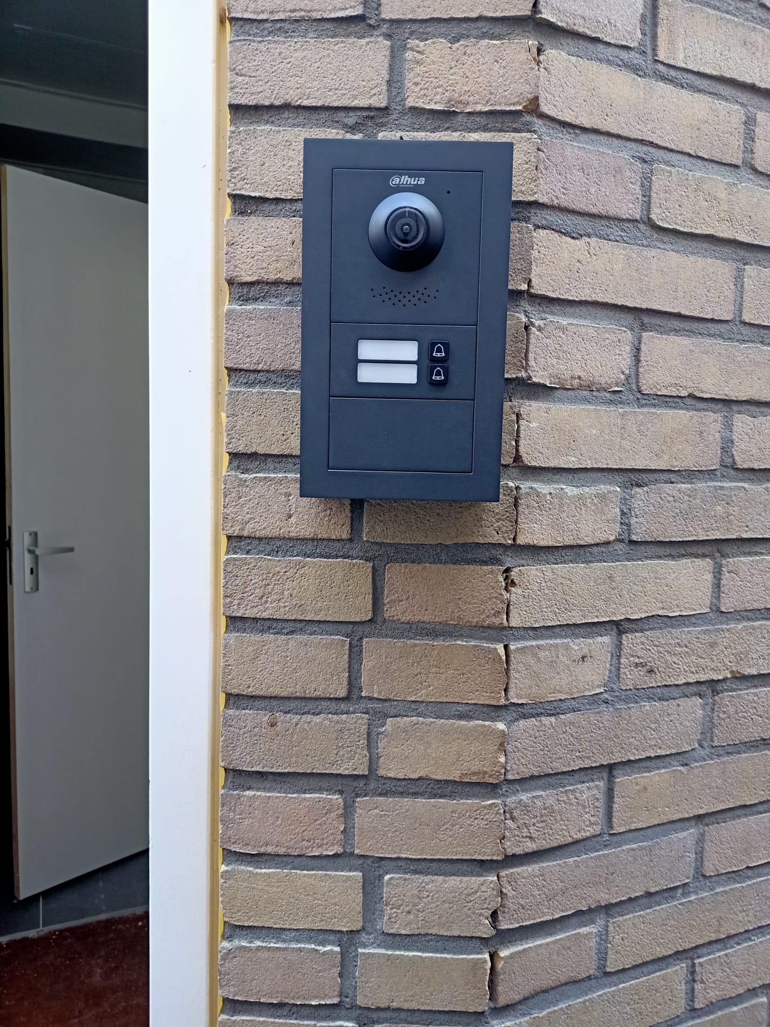 Video-intercom met twee belknoppen, opbouw gemonteerd op de bakstenen hoek naast de toegangsdeur van een bedrijfspand