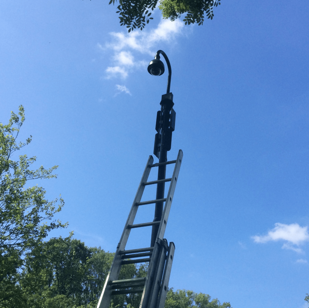Bestuurbare domecamera onder de arm van een lichtmast, met een ladder ertegenaan