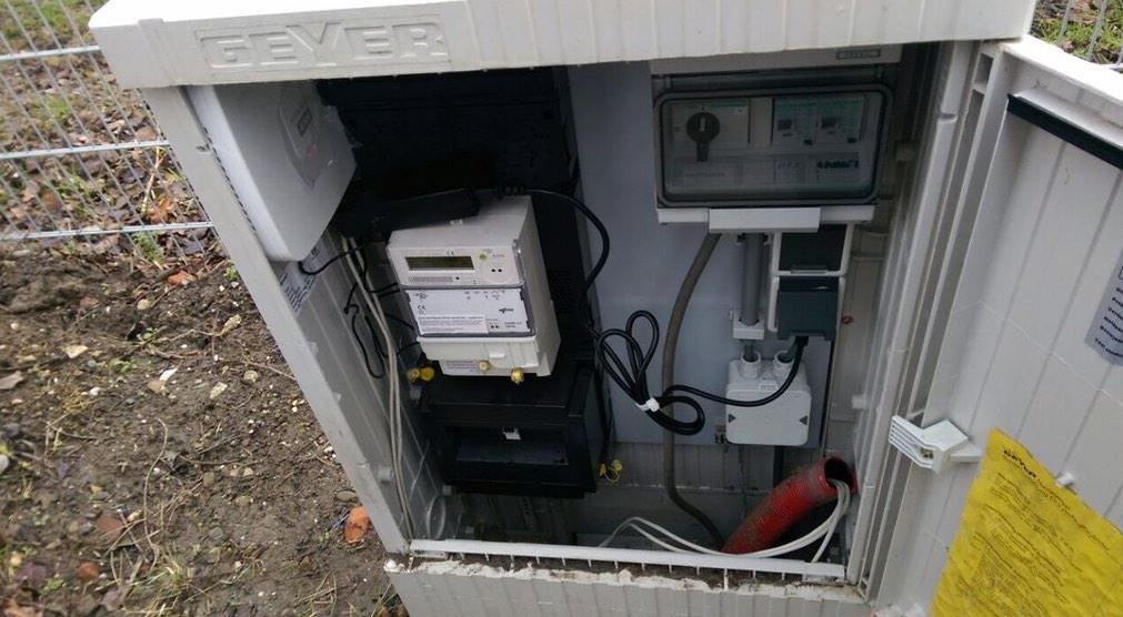 Open buitenkast langs een hek met kilowattuurmeter, verdeler met automaten en netwerkbekabeling