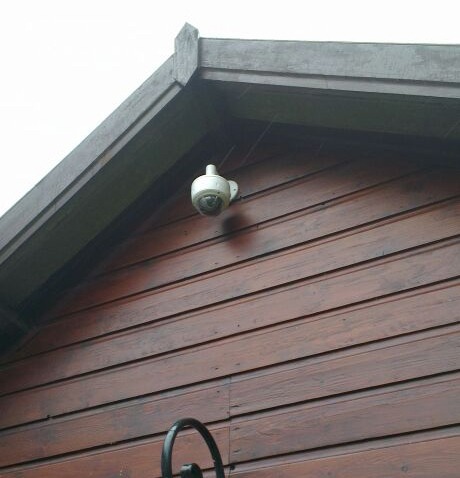 Witte bewakingscamera hoog onder de nok van een houten gevel