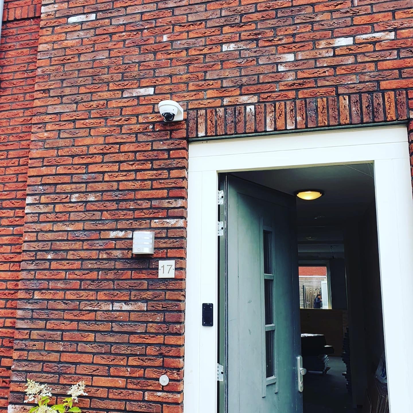 Compacte witte gevelcamera naast de voordeur van een bakstenen woning