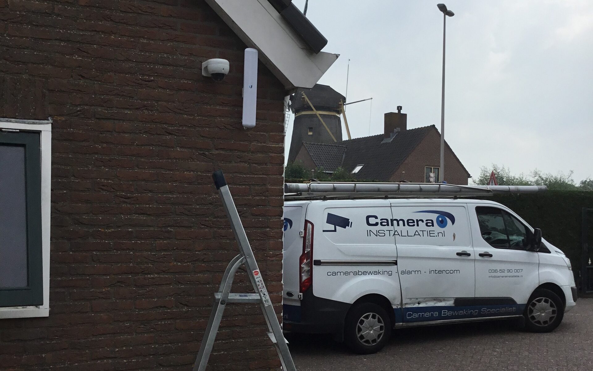Witte domecamera onder de dakrand, met onze servicebus ervoor