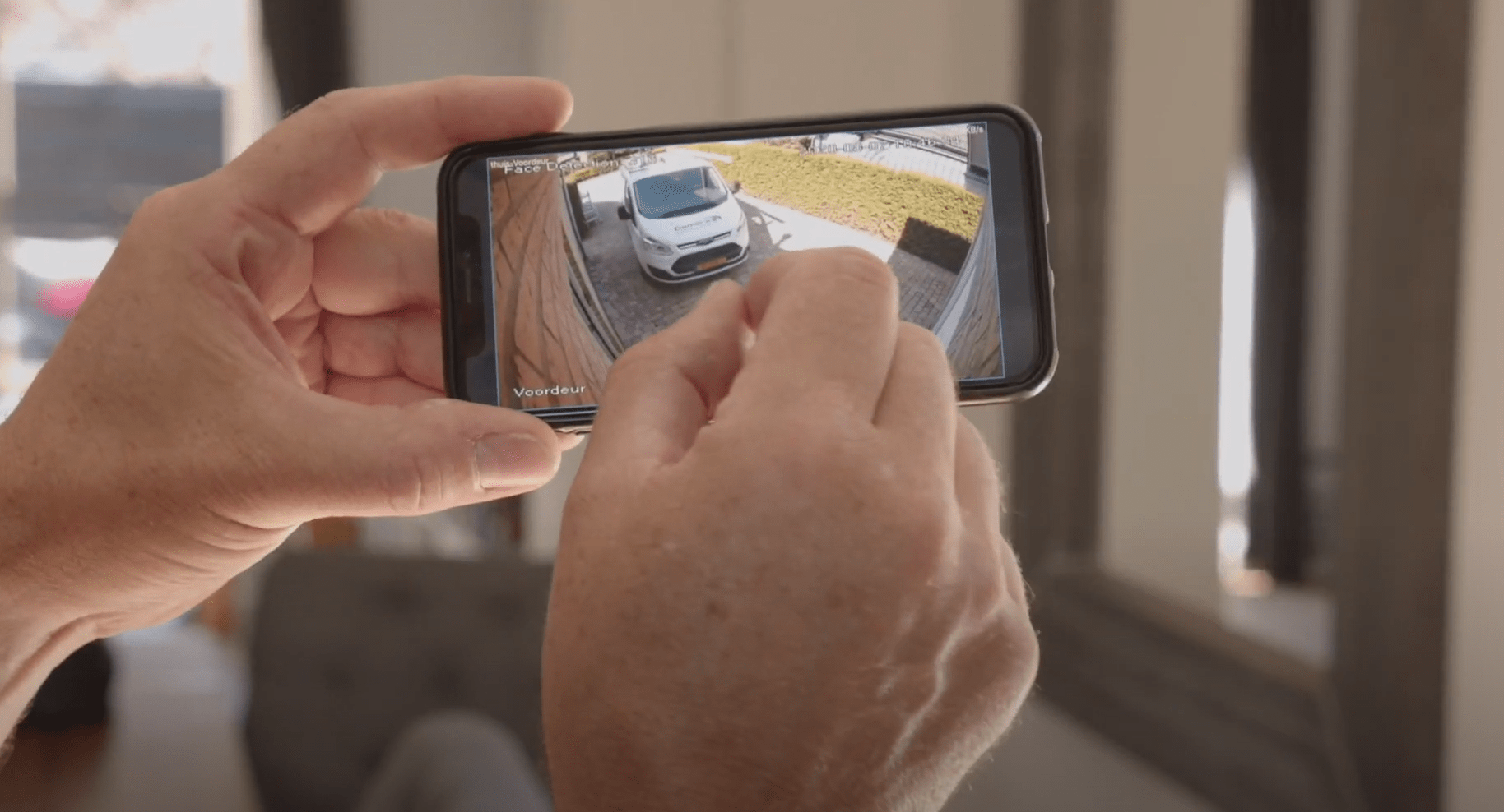 Hand houdt een telefoon vast waarop het live beeld van een buitencamera te zien is