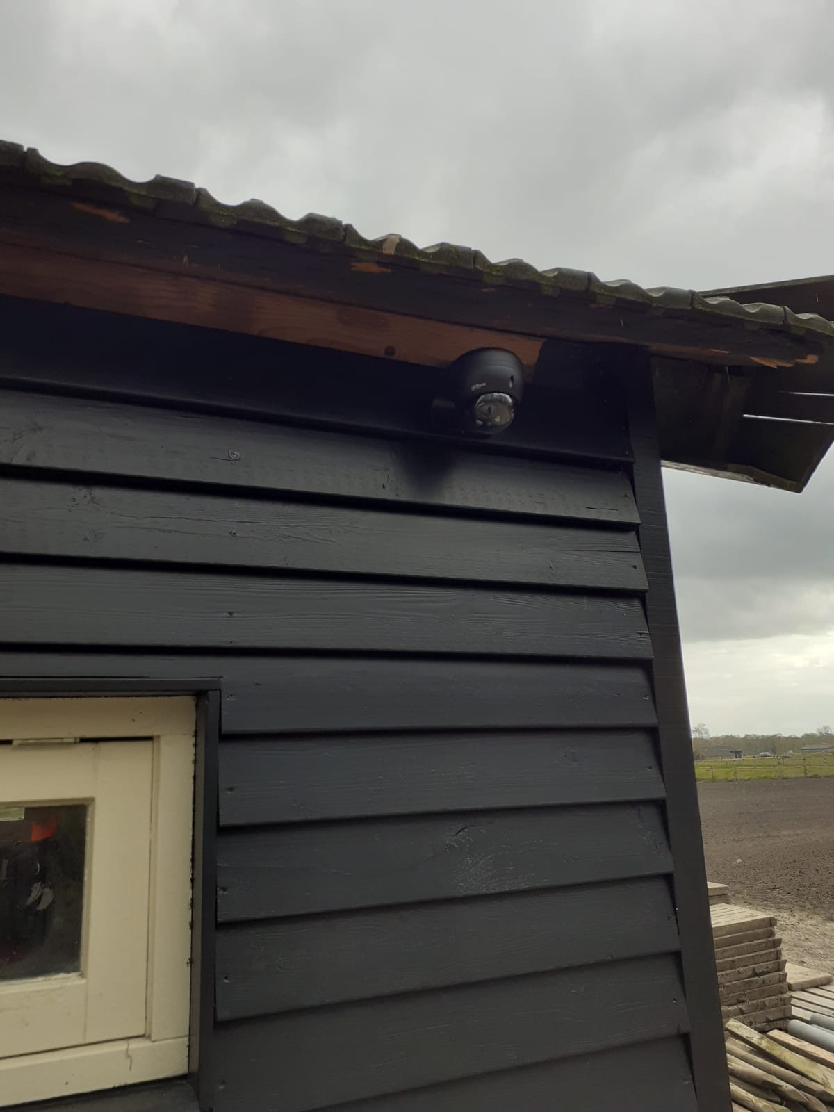 Zwarte camera onder de dakrand van een donker houten bijgebouw