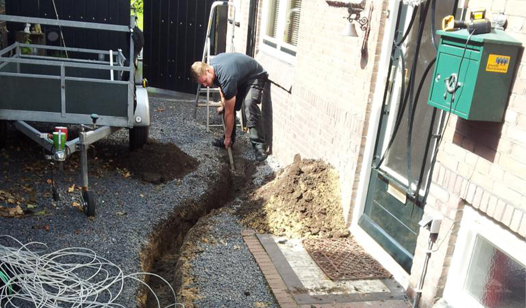 Monteur graaft een smalle sleuf langs het pad naast de woning voor de camerakabel