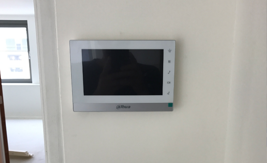 Wandmonitor van een video-intercom naast een deurpost binnen, met bedieningsknoppen langs de rechterzijde van het scherm