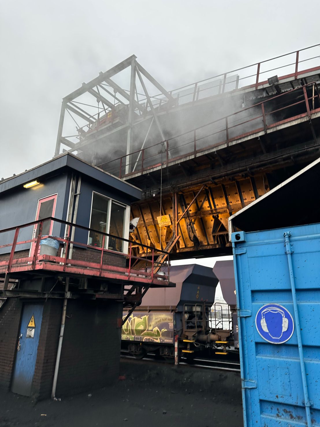 Laadbrug met bedieningscabine boven treinwagons op de bulkterminal, met stoom die van de installatie af komt