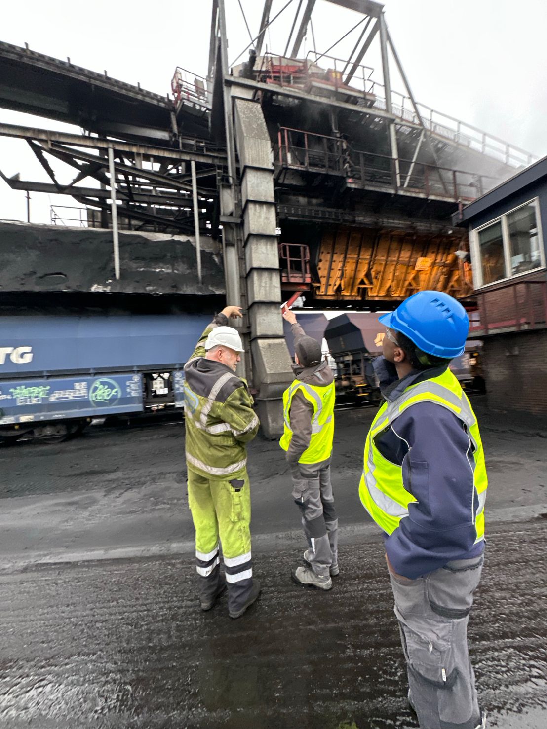 Monteurs in veiligheidskleding kijken omhoog naar de laadbrug van de bulkterminal, met treinwagons vol bulk op de achtergrond