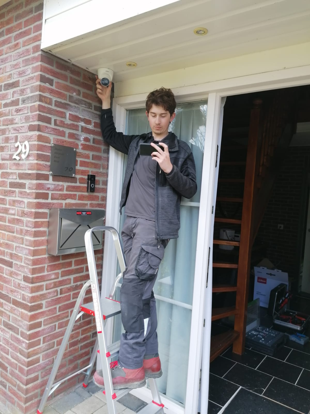 Monteur op een trapje houdt een domecamera bij het plafond van de entree