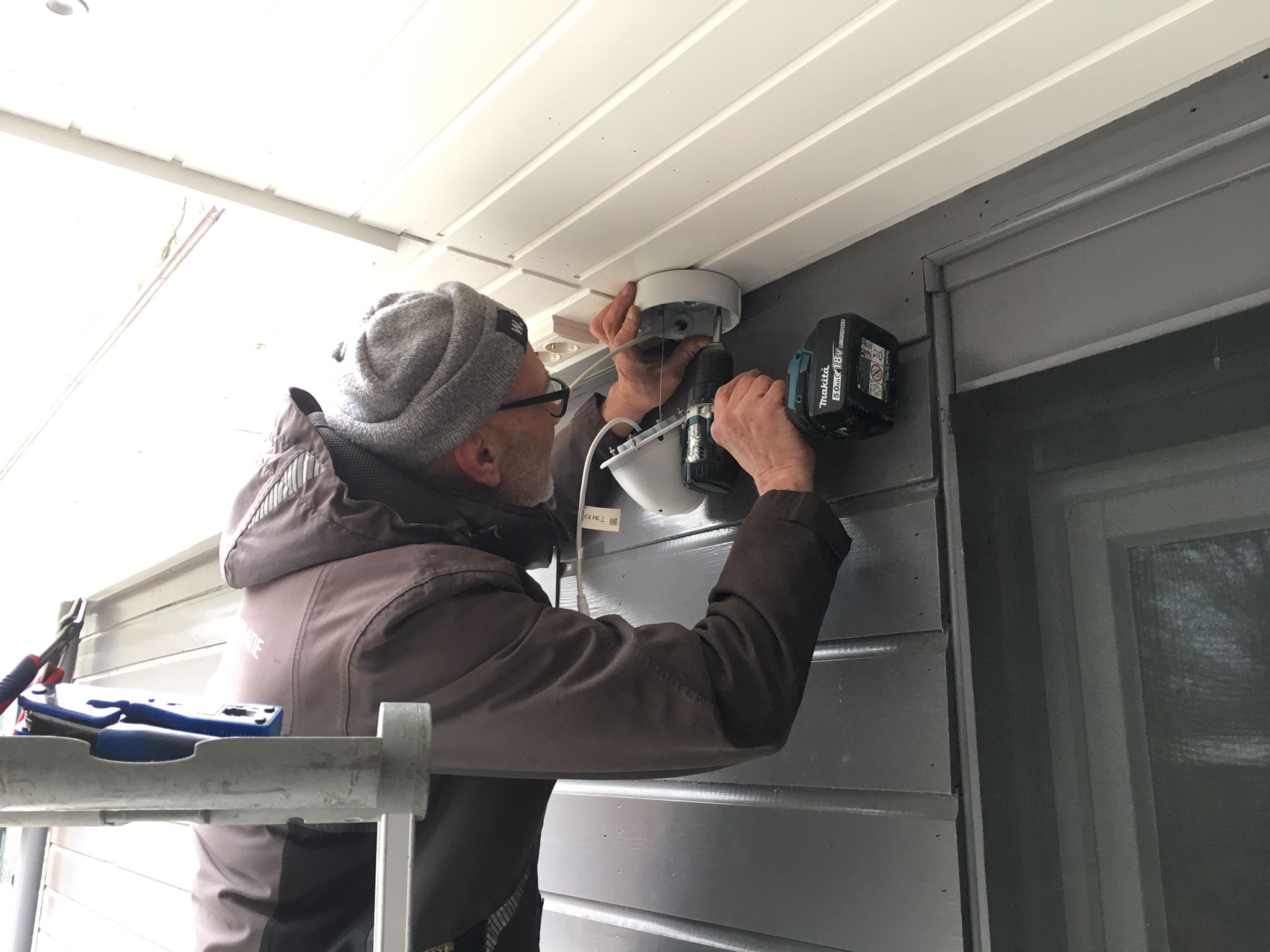 Monteur zet een dome-camera vast onder de dakrand van een woonhuis