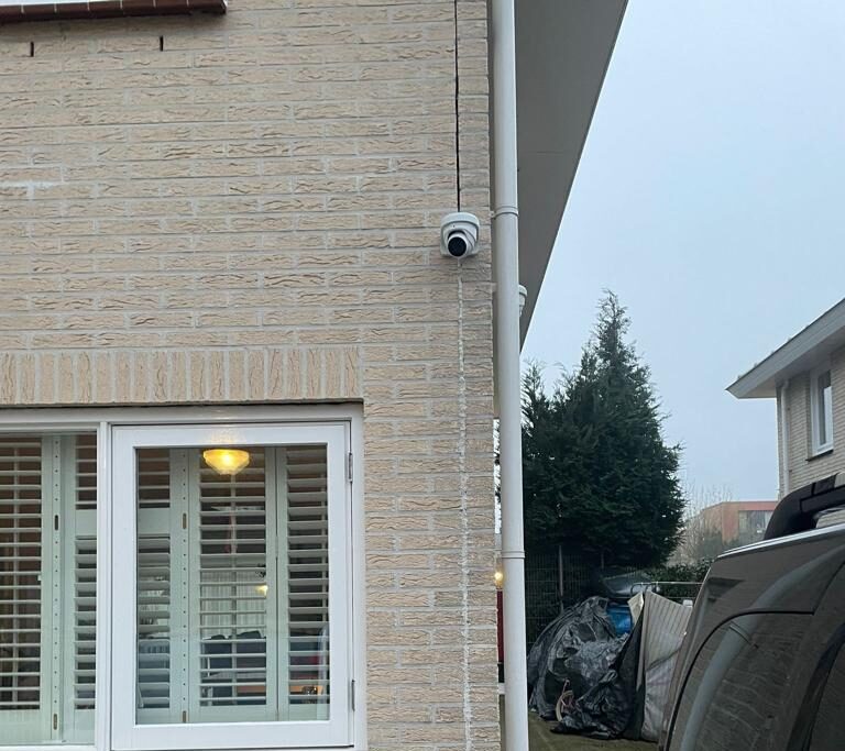 Witte domecamera hoog op de hoek van een woning van lichte baksteen, naast de regenpijp