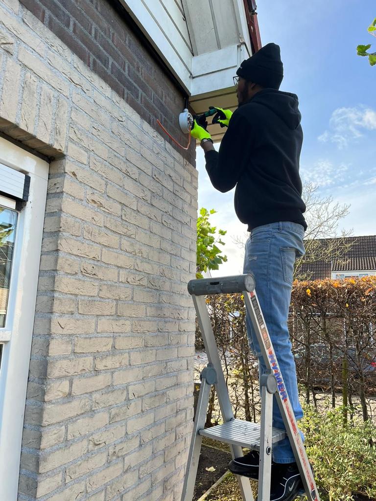 Monteur op een trap die een camera onder de dakrand van een gevel vastzet