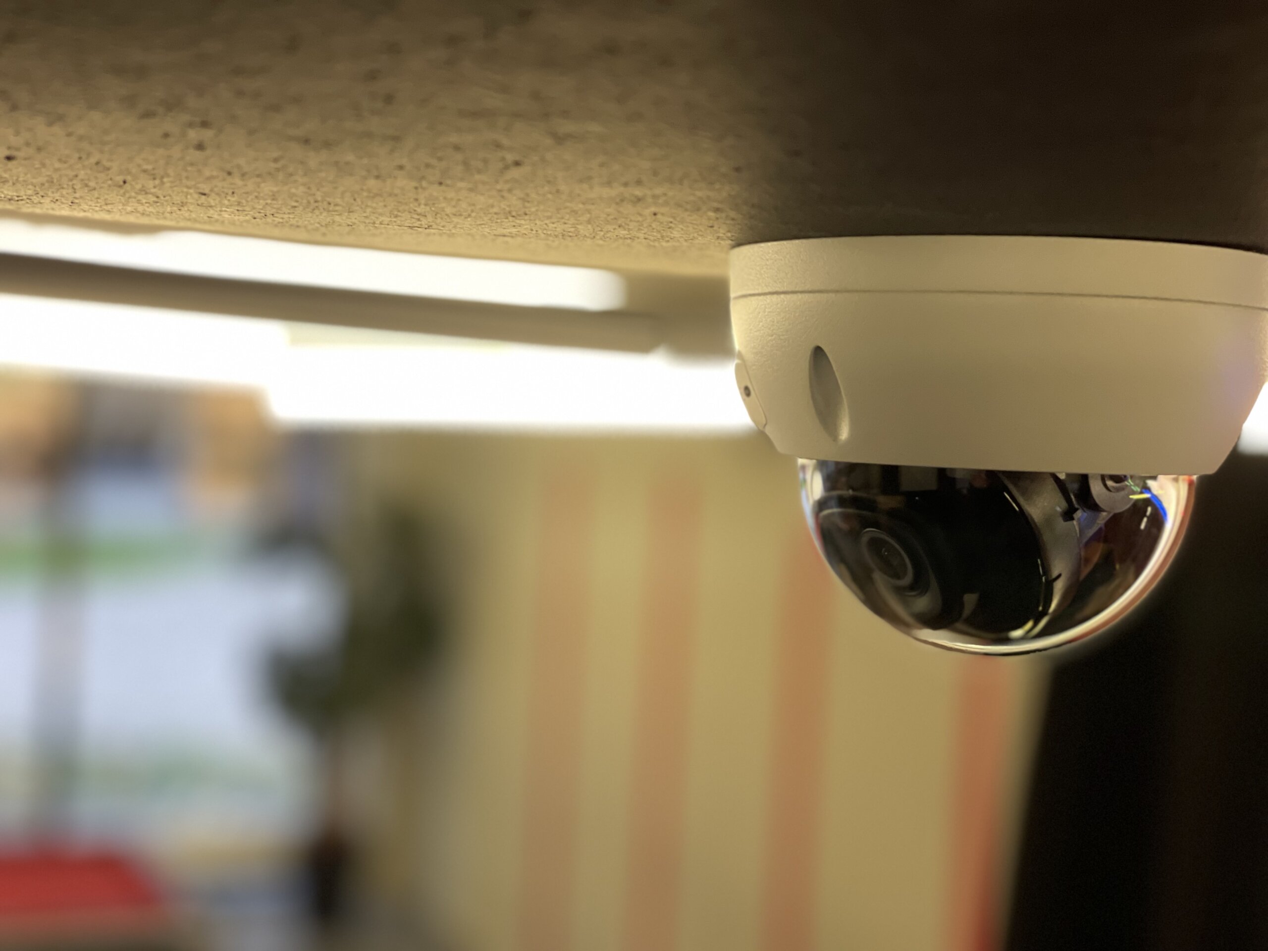 Witte domecamera strak tegen een betonnen plafond bij de entree van een appartementengebouw