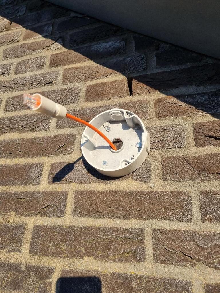 Ronde witte montagevoet op een bakstenen gevel met de oranje netwerkkabel door het midden