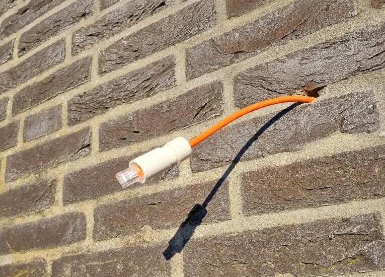 Oranje netwerkkabel met RJ45-connector komt netjes uit een bakstenen buitengevel, klaar om op een camera te worden aangesloten