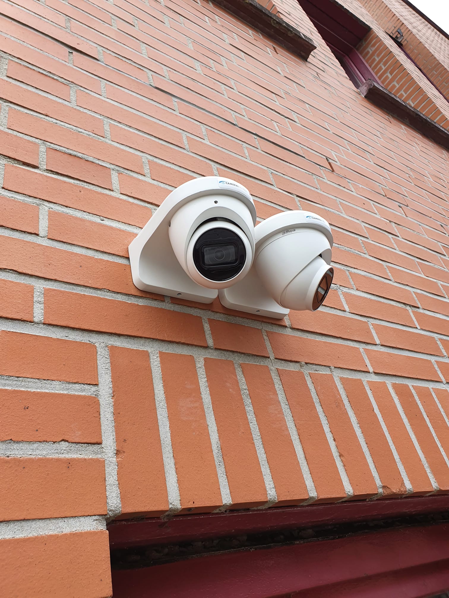 Twee witte Dahua-camera's samen op een beugel tegen een rode bakstenen gevel, elk met een eigen kijkrichting