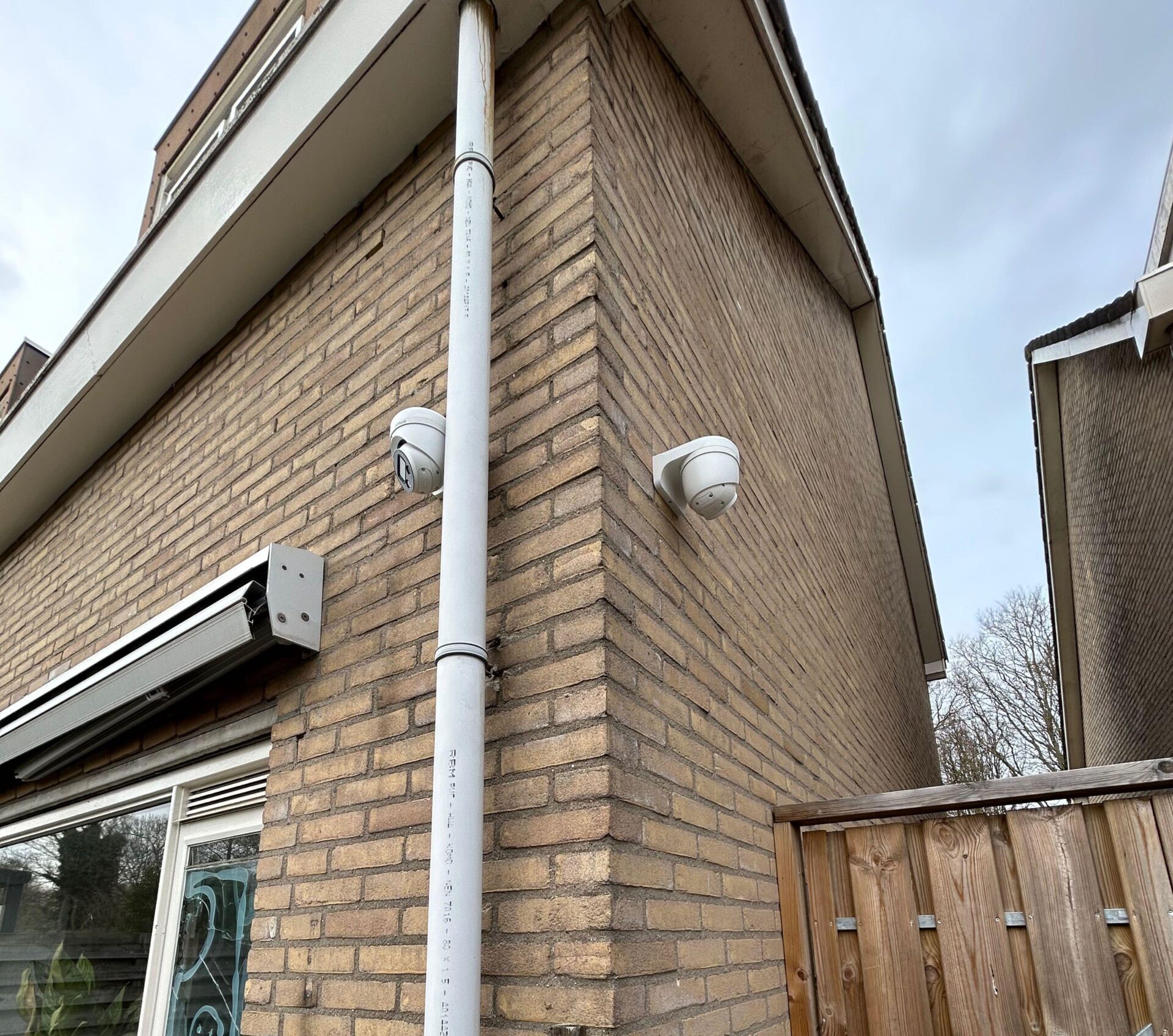 Twee witte camera’s op de bakstenen gevelhoek van de woning, elk een andere kant op gericht