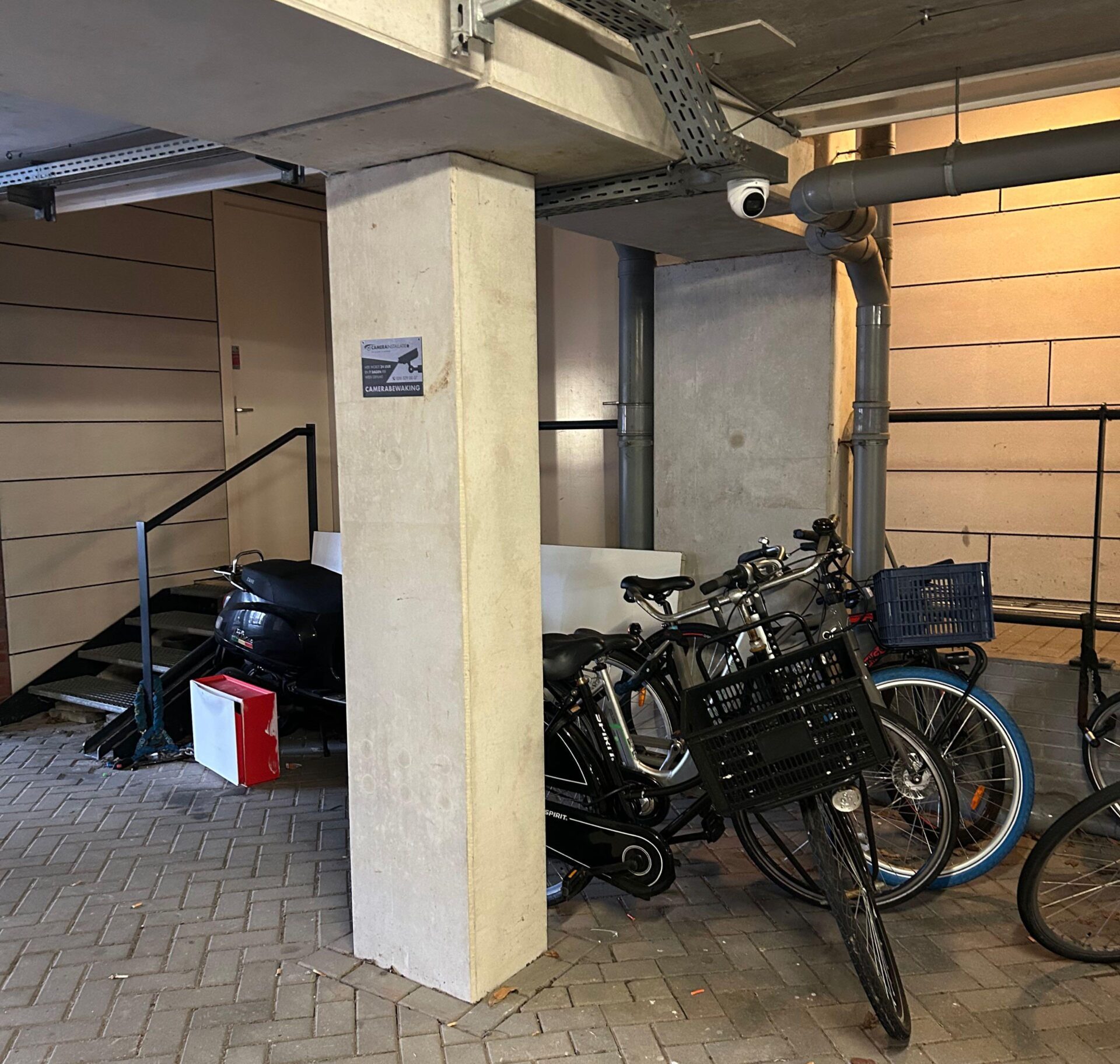 Overdekte fietsenstalling met fietsen en een scooter, met een camera aan het plafond