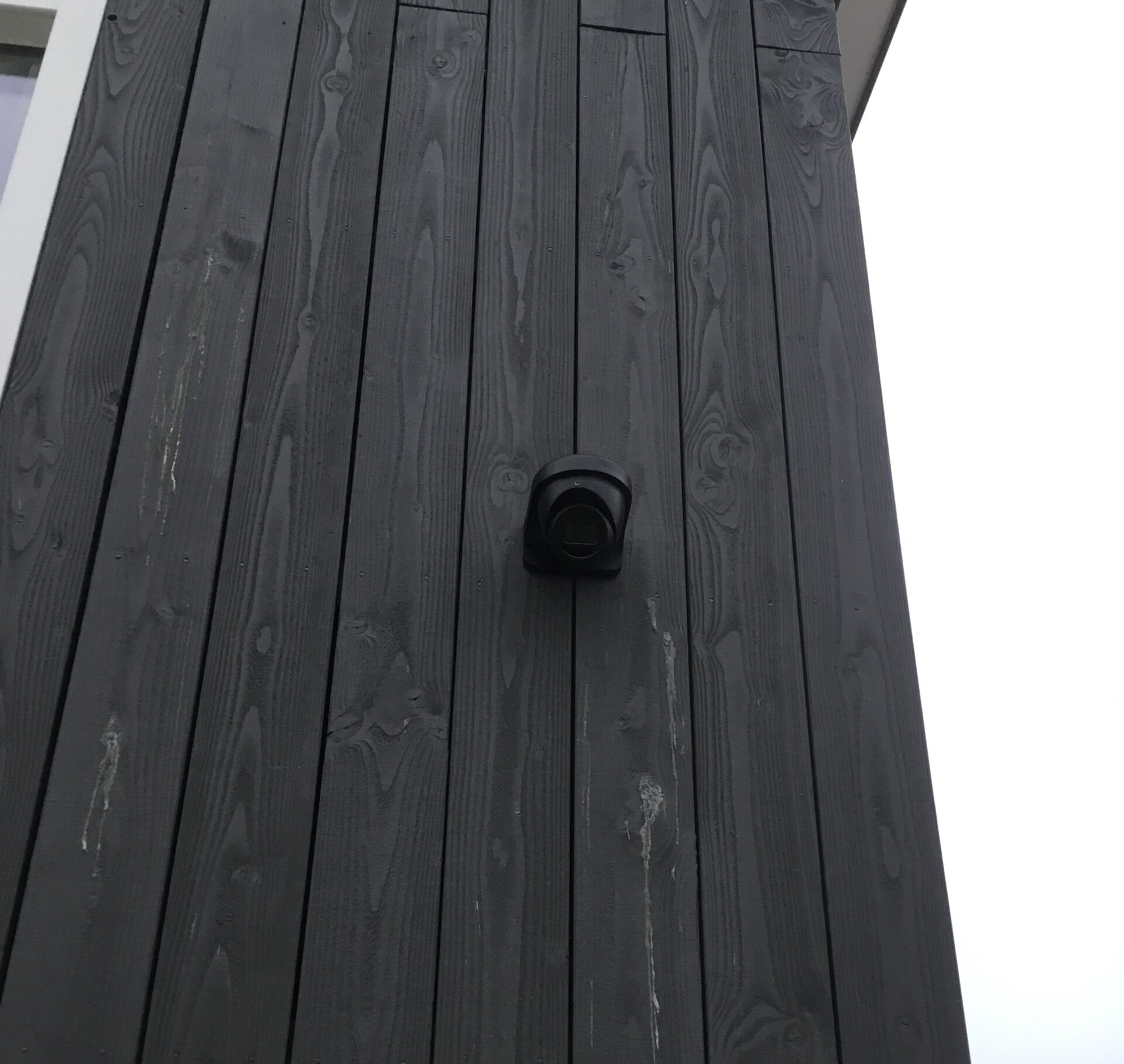 Zwarte turret-camera strak gemonteerd op de zwarte houten gevel van de woning, met zicht op de omgeving