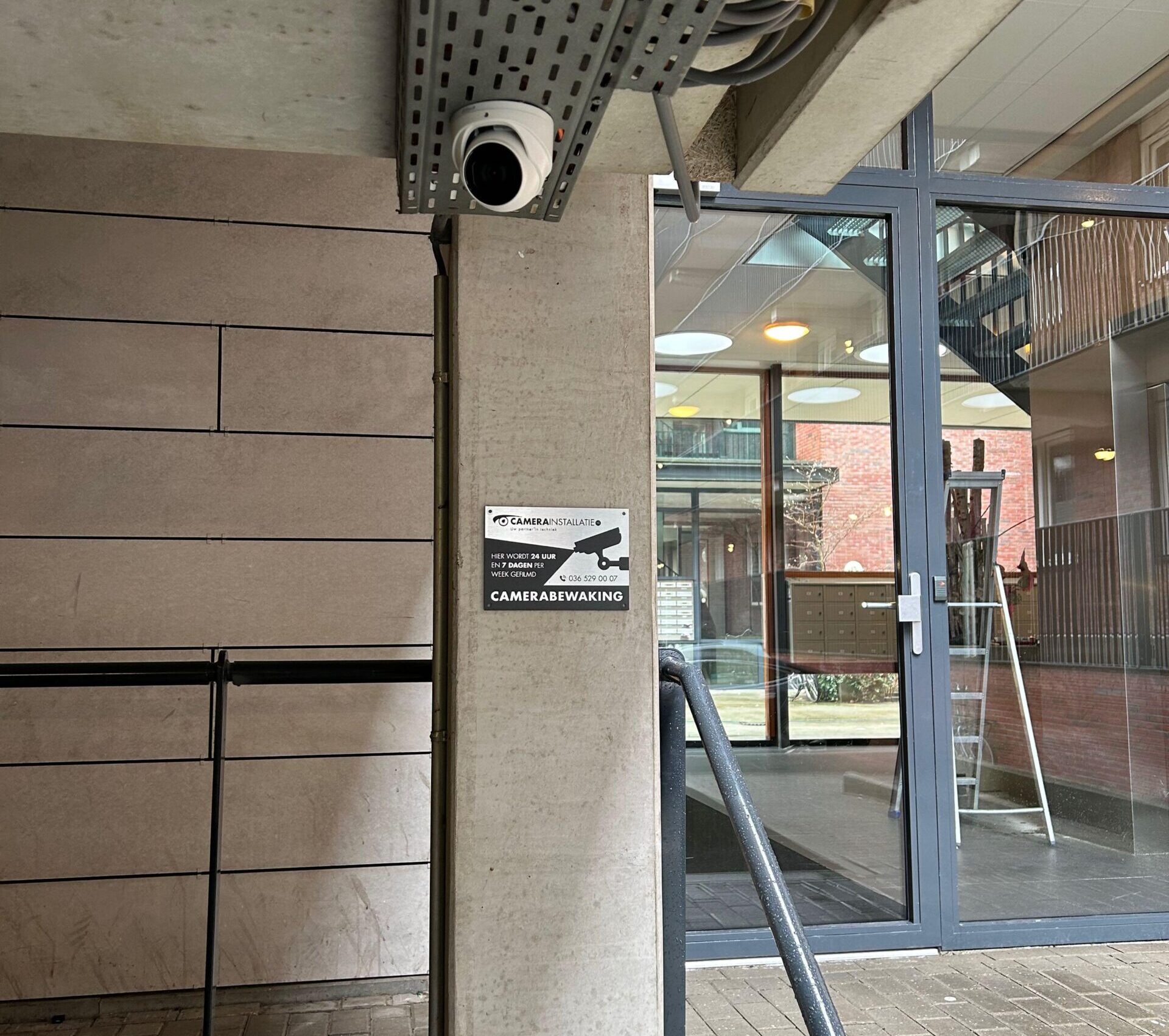 Camera onder een kabelgoot bij de ingang, met daaronder het bordje camerabewaking