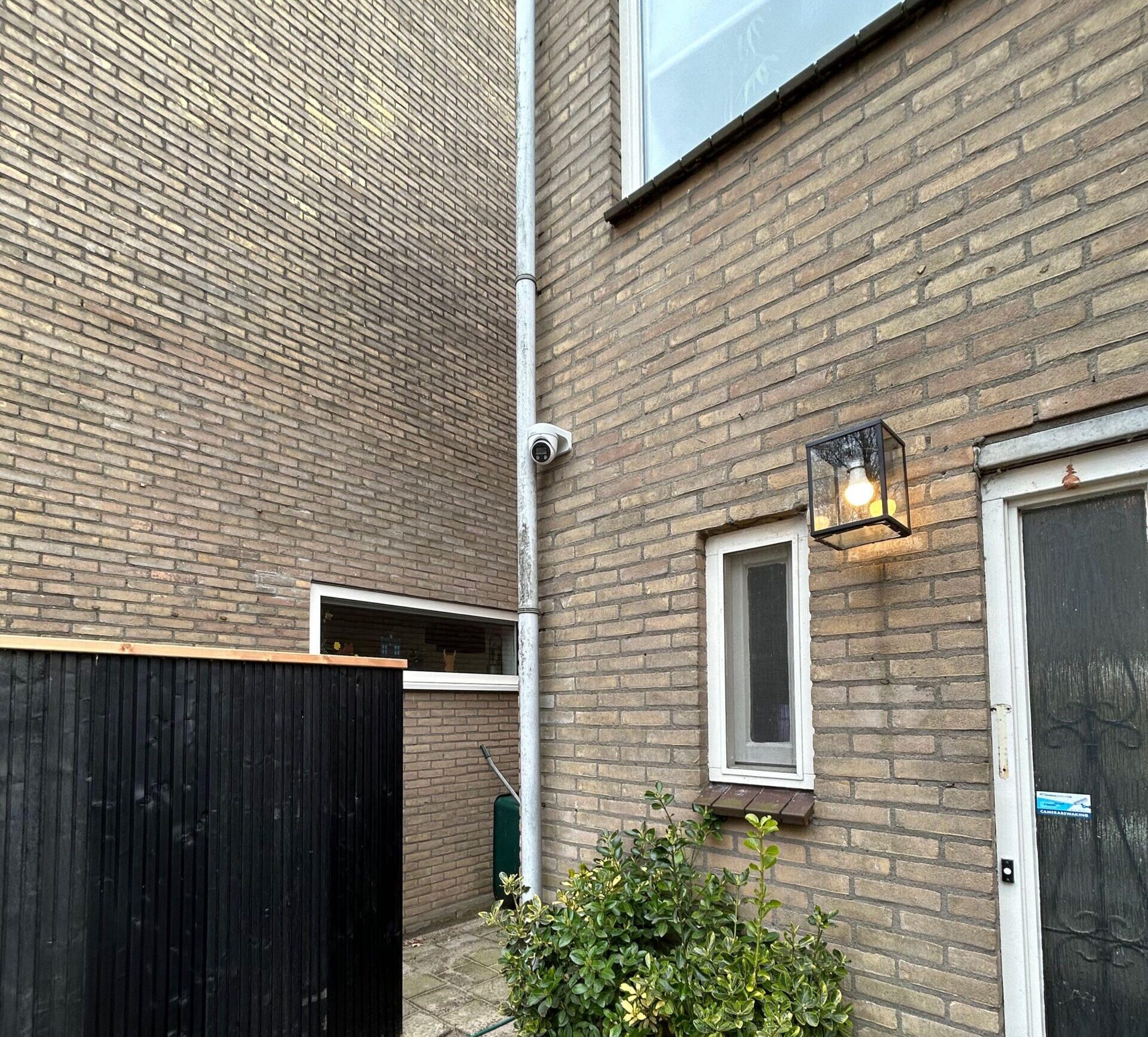 Witte camera hoog tegen de zijgevel, boven het smalle pad tussen twee woningen