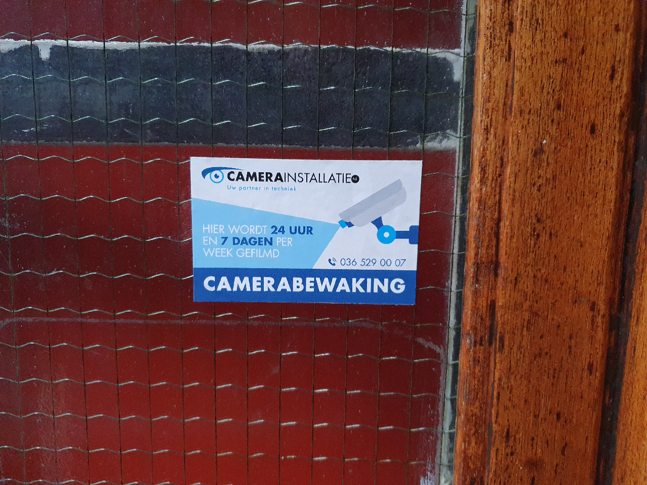 Bordje van CameraInstallatie.nl op een deur, met de tekst dat er zeven dagen per week gefilmd wordt