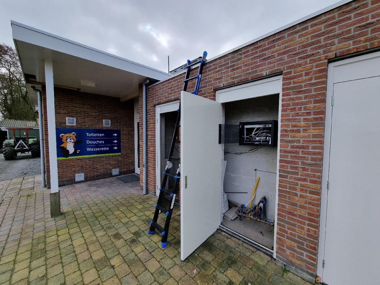 Sanitairgebouw van een camping met camerabewaking en een open technische kast met patchkast