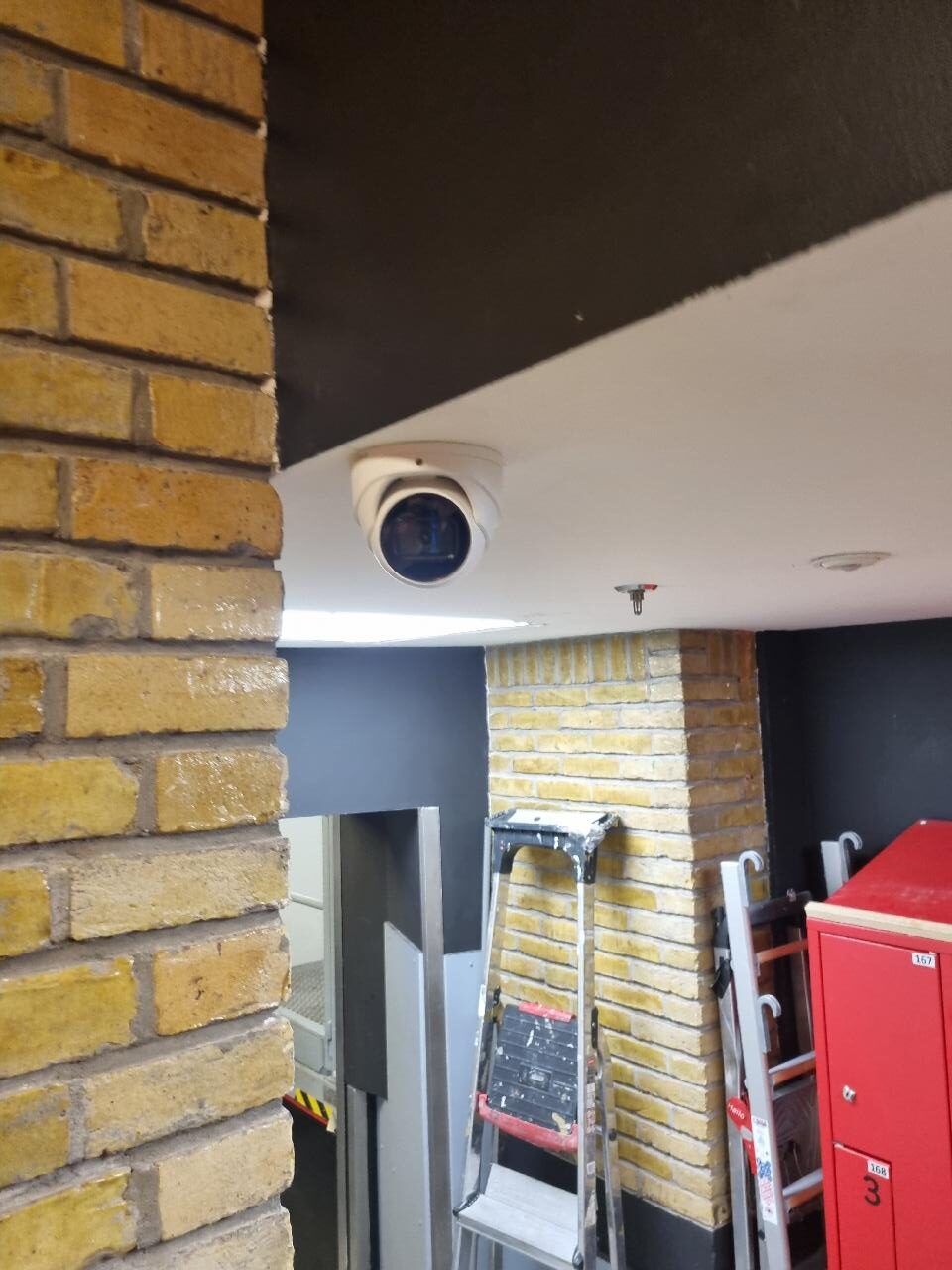 Domecamera aan het plafond bij de entree van een hotel, naast de brandslanghaspel