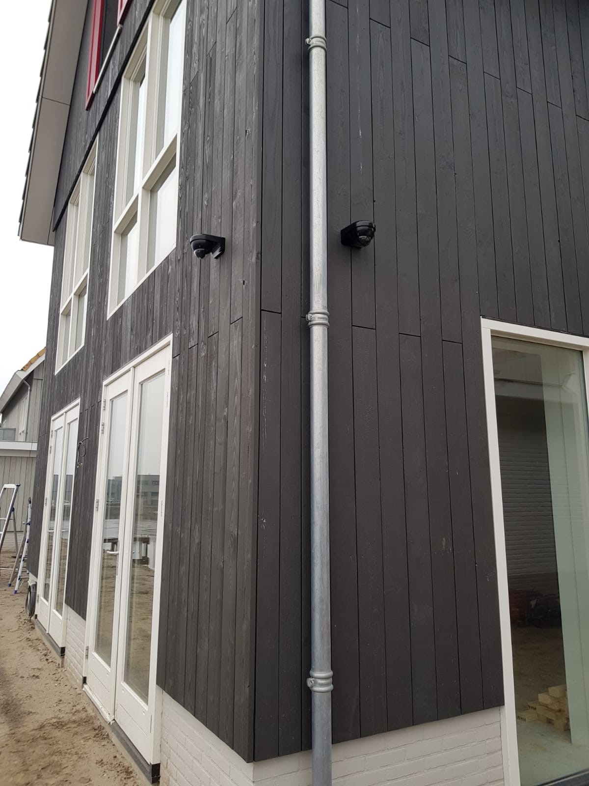 Twee zwarte dome-camera's, in kleur afgestemd op de donkere houten gevel van een moderne woning, rond een hoek geplaatst
