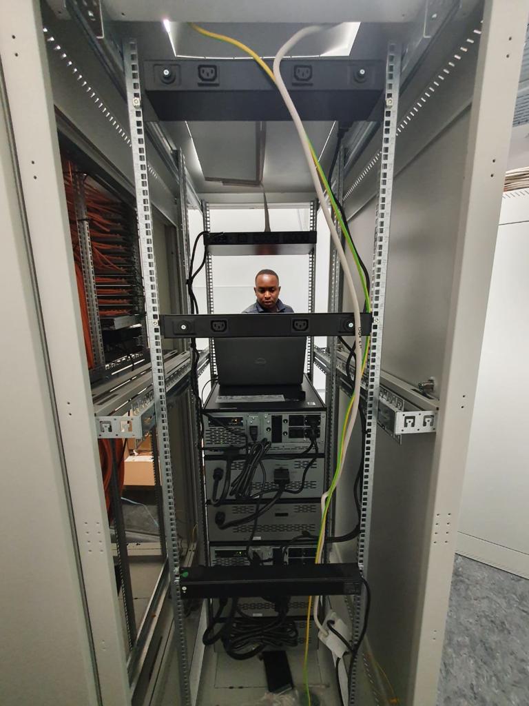 Monteur van CameraInstallatie.nl werkt met een laptop in een open serverrack met patchpanelen en voedingen