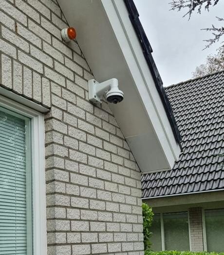 Bestuurbare domecamera op een muurbeugel onder de dakrand van een woning, met daarboven een oranje buitensirene
