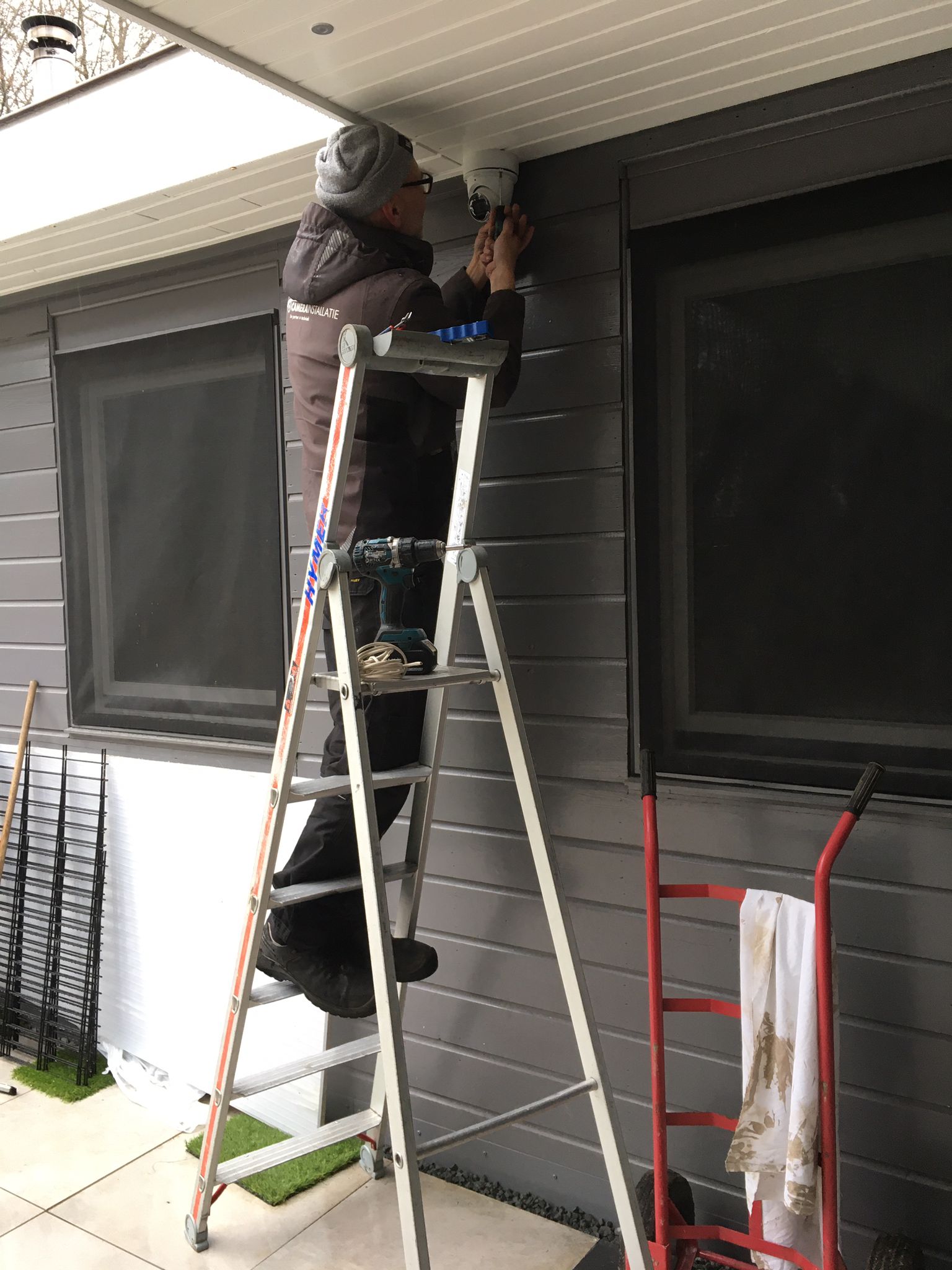 Trap tegen de grijze gevel van het chalet terwijl de camera bij de dakrand wordt geplaatst