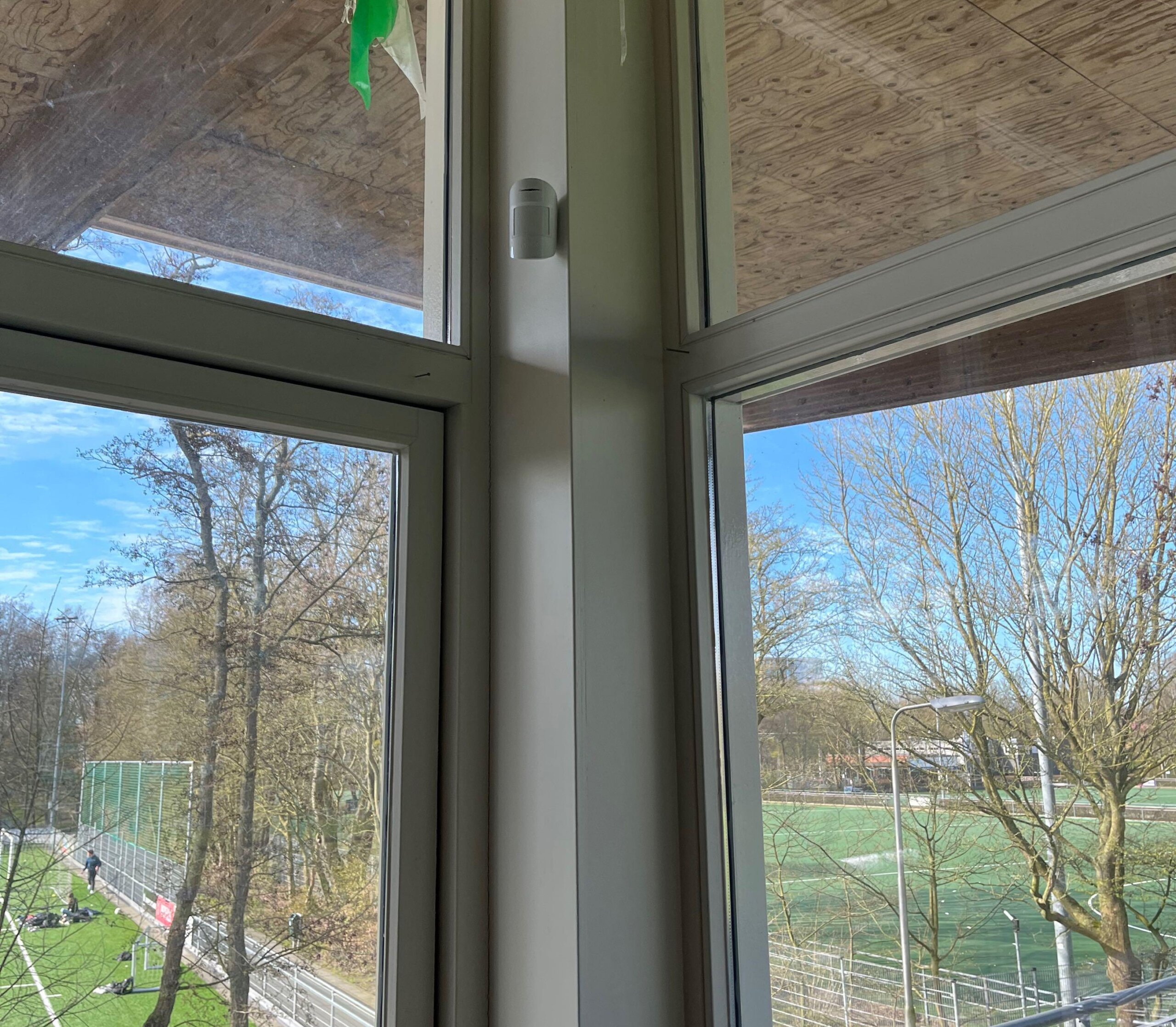 Melder bij een raampartij met uitzicht op het buitenterrein van een clubgebouw