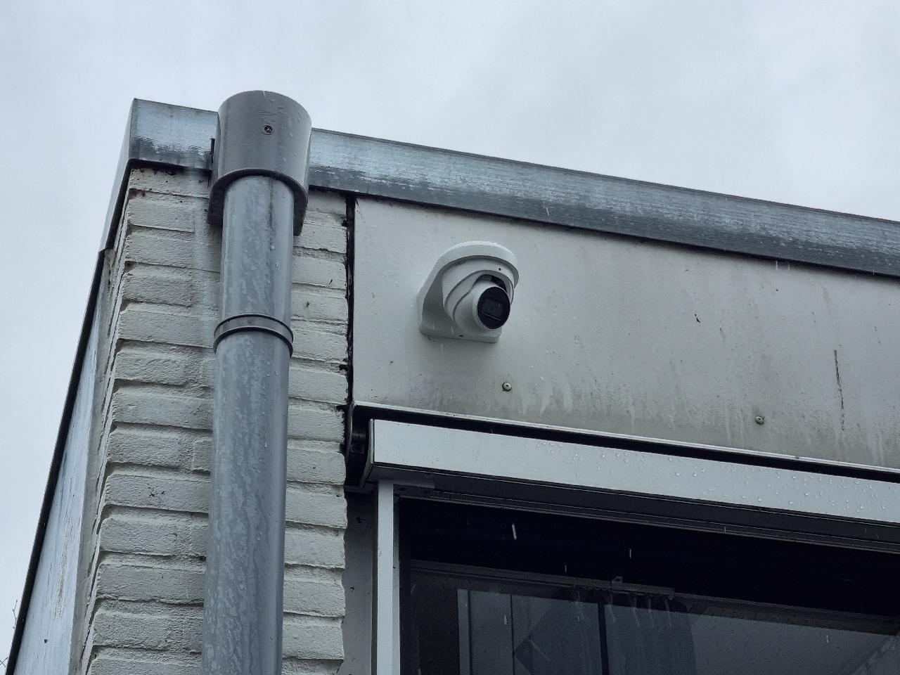 Domecamera onder de dakrand van het schoolgebouw, naast een zinken regenpijp