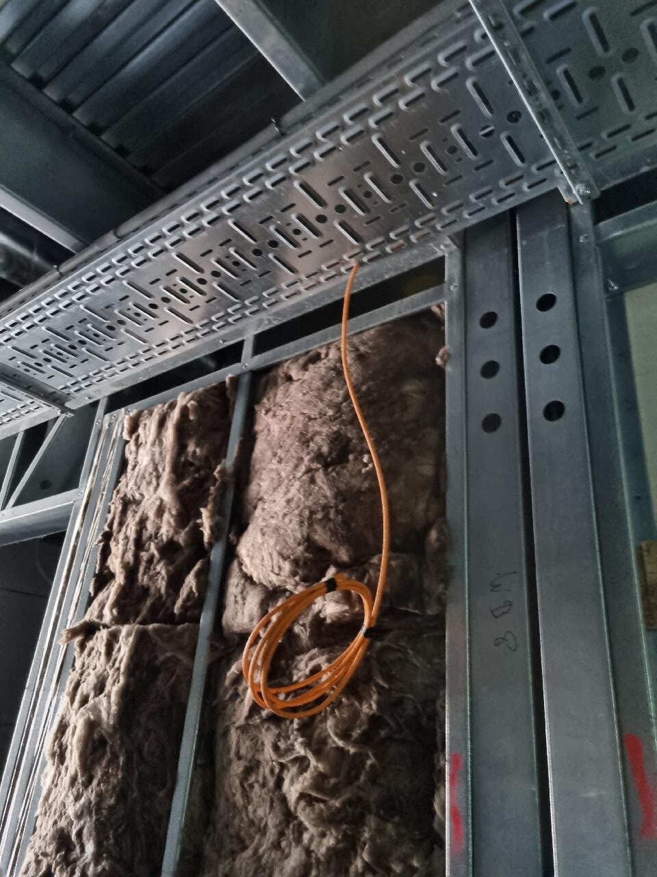 Close-up van oranje netwerkkabels die over een metalen kabelgoot langs staalconstructie lopen